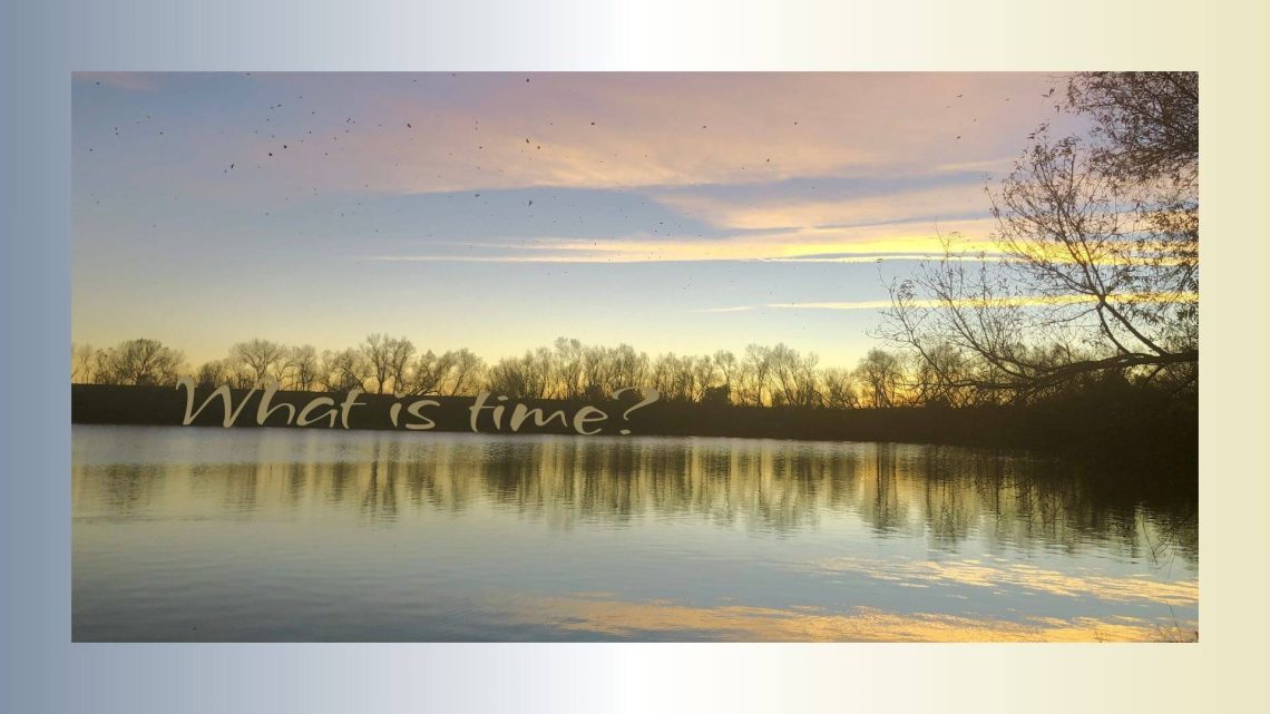 A still lake reflecting the soft golden and lavender hues of the evening sky, with bare trees silhouetted along the horizon. The text on the image reads: “What is time?”