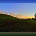 A grassy hillside at sunset with a winding dirt path and silhouetted trees against the fading light. The text overlay reads, “What is God?”