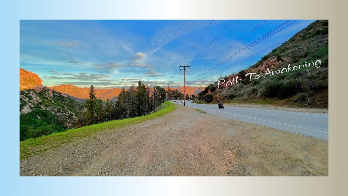 A winding mountain road at sunset with motorcycles riding along, surrounded by hills and a wide sky with scattered clouds. The text on the image reads, “Path To Awakening.”